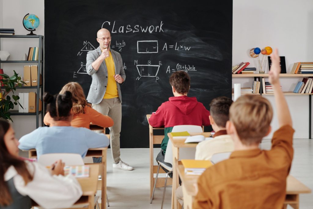 a person standing in front of a classroom with a blackboard