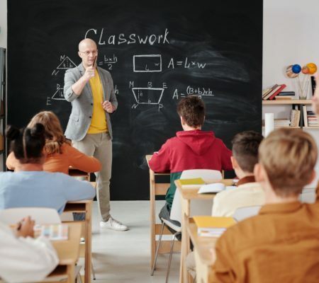 a person standing in front of a classroom with a blackboard