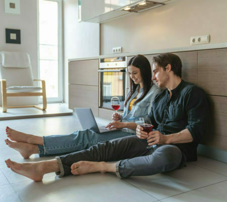 a man and a woman sitting on the floor with a laptop and a glass of wine