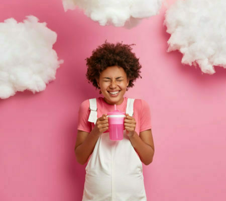 Overjoyed pregnant woman holds bottle with water smiles broadly going to give birth to child dressed in casual clothes has big abdomen poses against pink background. Pregnancy maternity concept