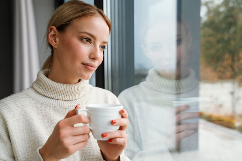 woman-drinking-coffee-while-leaning-on-window-glass