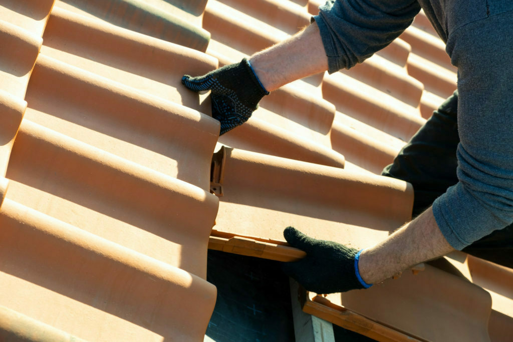 worker-hands-installing-yellow-ceramic-roofing-tiles-mounted-on-wooden-boards-covering