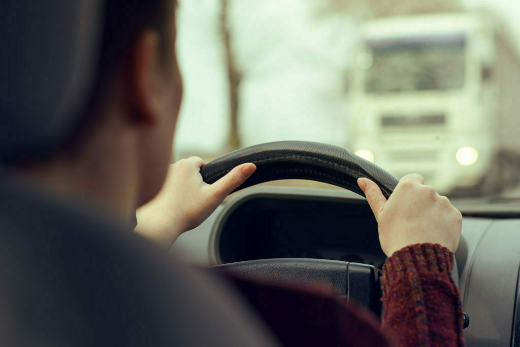 Woman driving car toward a large truck on the road