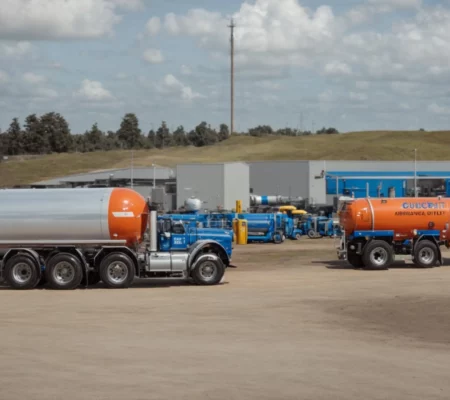a row of fuel trucks, each marked with a different type of fuel, is parked neatly outside a local fuel supply depot under a clear blue sky.